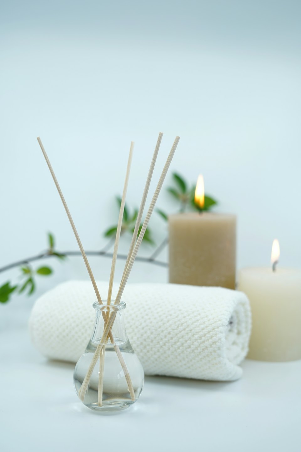 Reed diffuser, rolled towel, and lit candles for wellness.