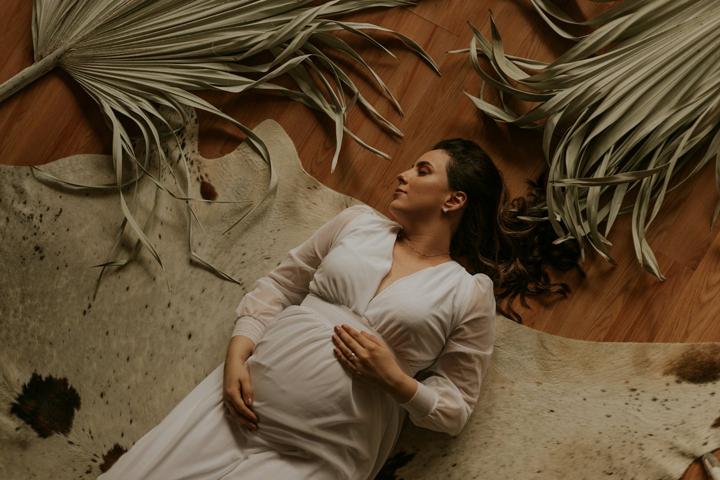 Pregnant woman in white dress lying on a cowhide rug.